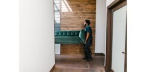 Professional mover carrying a sofa during a home relocation in Dubai, next to a junk removal team clearing unwanted items
